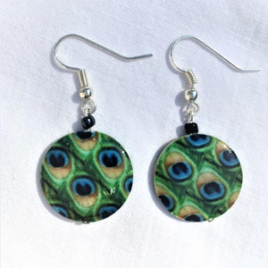 May include: A pair of silver dangle earrings with round, green, blue, and black peacock feather patterned charms.