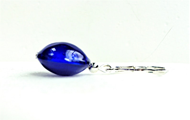 Pu&ograve; includere: Un orecchino a goccia di vetro blu scuro con un gancio d'argento.