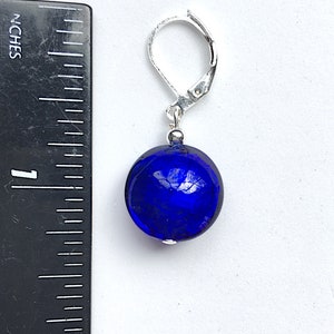 Pu&ograve; includere: Un paio di orecchini in vetro blu con chiusura a leva argentata. Gli orecchini sono rotondi e hanno una superficie testurizzata.