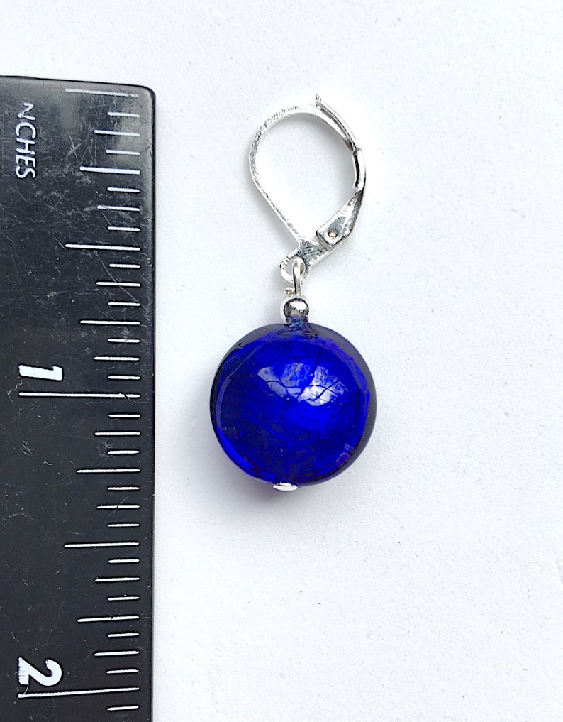 Pu&ograve; includere: Un paio di orecchini in vetro blu con chiusura a leva argentata. Gli orecchini sono rotondi e hanno una superficie testurizzata.
