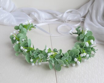 May include: A green and white floral crown made of artificial greenery and small white flowers.