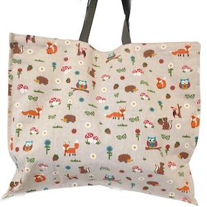 May include: A large beige tote bag with a grey handle. The bag is decorated with a repeating pattern of foxes, owls, squirrels, hedgehogs, mushrooms, and flowers.