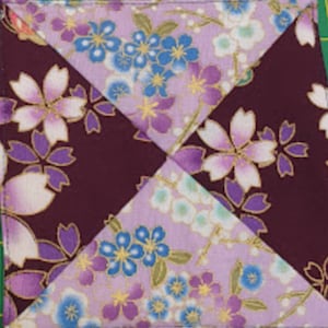 May include: A square fabric coaster with a patchwork design. The coaster is made of four different fabrics, each with a floral pattern. The fabrics are in shades of purple, pink, white, and blue.