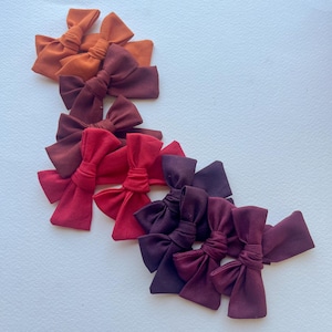 May include: A set of ten fabric hair bows in shades of orange, red, and purple. The bows are arranged in a gradient from orange to purple.