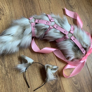 Può includere: Una coda in finta pelliccia grigia e bianca, abbinata a un'imbracatura e un nastro rosa. Un cerchietto abbinato con dettagli a forma di orecchie completa il set. Ideale per cosplay o costumi.
