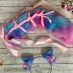 Può includere: Una coda di pelliccia sintetica rosa e blu con un nastro rosa e una fascia per capelli abbinata con orecchie di pelliccia sintetica. La coda è legata con un cordoncino rosa.