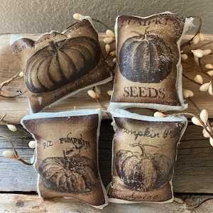 May include: Four small burlap pillow ornaments with a vintage pumpkin design. Each pillow features a different pumpkin design and text, including "Pumpkin Seeds", "Pie Pumpkin", and "Pumpkin Spice".