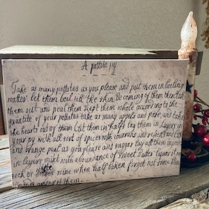 May include: A vintage recipe card with handwritten instructions for making a "pottile py." The card is cream-colored with black ink and features a small star in the top right corner. The recipe includes ingredients like potatoes, apples, pears, spices, currants, raisins, and orange peel.