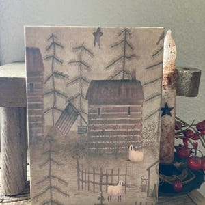 May include: A vintage-style illustration of a rustic cabin with a red roof and a white picket fence. Two white sheep are in the foreground, and a small American flag hangs from the cabin. The background features a forest of pine trees and a star in the sky.