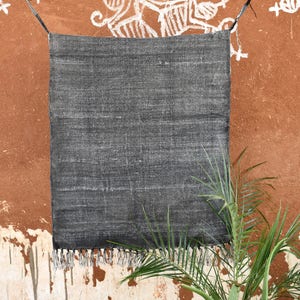 May include: A black woven rug with fringe hanging on a wall with white drawings. The rug is made of natural fibres and has a textured surface.
