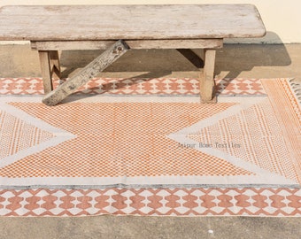 May include: A white and orange patterned rug with fringe on the edges. The rug has a geometric design with a white background and orange accents. A wooden bench is sitting on top of the rug. The rug has the text "Jaipur Home Textiles" printed on it.