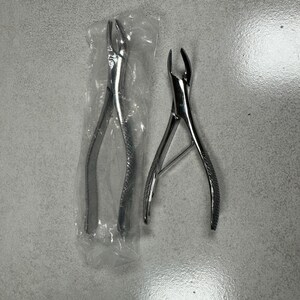 May include: Two stainless steel dental extraction forceps. One is sealed in a clear plastic bag. The forceps have curved beaks and textured handles for grip. The tools are designed for dental procedures.
