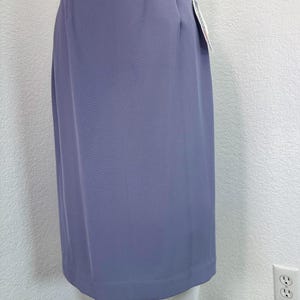May include: A periwinkle-colored skirt with a straight silhouette. The skirt has a simple design with a clean, tailored look. A tag is attached to the side. The skirt is made of a smooth, solid fabric.