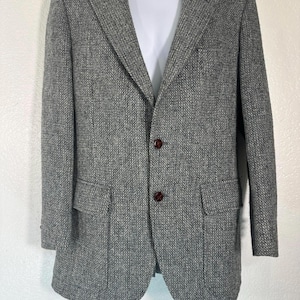 May include: A gray tweed blazer with two front pockets and two brown buttons. The blazer is displayed on a white mannequin. The fabric has a textured appearance.