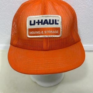 May include: A white ceramic mug with a black handle and the text "But First, Coffee" in a bold, black font. The mug is set against a blurred background, suggesting a cozy setting.