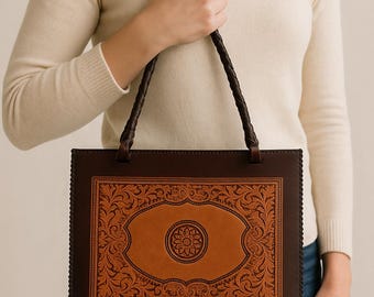 May include: A rectangular brown leather tote bag with a decorative floral design in the center. The bag has a dark brown border and braided handles. The central design is a lighter shade of brown.