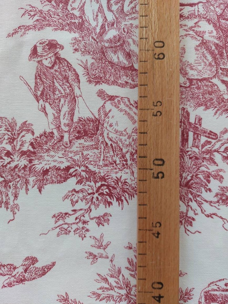 May include: Red and white toile fabric with a repeating pattern of a boy walking a sheep, trees, and birds. A wooden ruler is visible on the right side of the image.