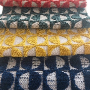 May include: Four different patterned rugs stacked on top of each other. The top rug is red, the second is green, the third is yellow, and the bottom rug is blue.