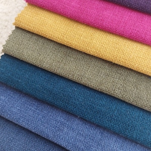 May include: A close-up of a stack of fabric swatches in various colors, including teal, blue, green, yellow, pink, and purple. The fabric has a textured, fuzzy surface.