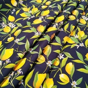 K&ouml;nnte beinhalten: Dunkelblauer Stoff mit einem sich wiederholenden Muster aus gelben Zitronen, gr&uuml;nen Bl&auml;ttern und kleinen wei&szlig;en Bl&uuml;ten. Der Stoff ist gefaltet und zeigt die Textur und das Design. Das Design erinnert an einen Sommergarten.