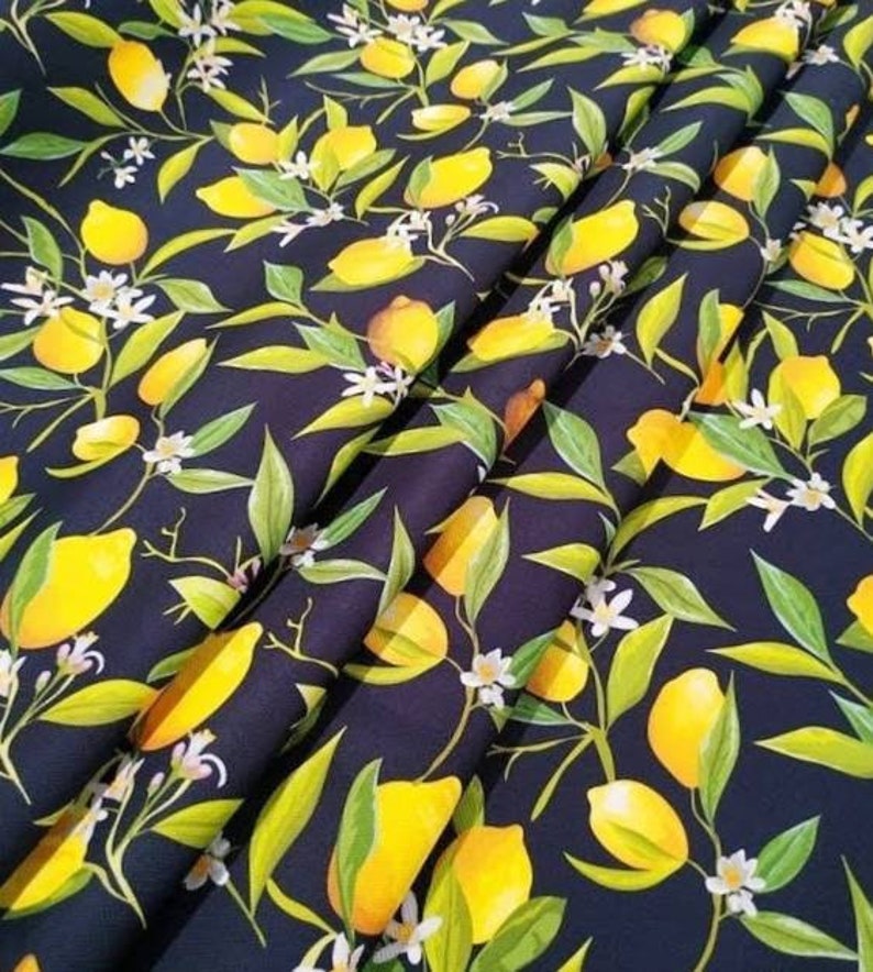K&ouml;nnte beinhalten: Dunkelblauer Stoff mit einem sich wiederholenden Muster aus gelben Zitronen, gr&uuml;nen Bl&auml;ttern und kleinen wei&szlig;en Bl&uuml;ten. Der Stoff ist gefaltet und zeigt die Textur und das Design. Das Design erinnert an einen Sommergarten.