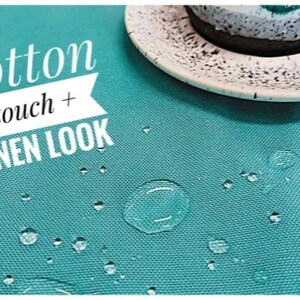 Op de afbeelding: Een close-up van een turquoise tafelkleed met waterdruppels. De tekst "cotton touch + LINEN LOOK" staat in het wit. Een witte schotel met een zwart gespikkelde rand en een kopje zijn zichtbaar.