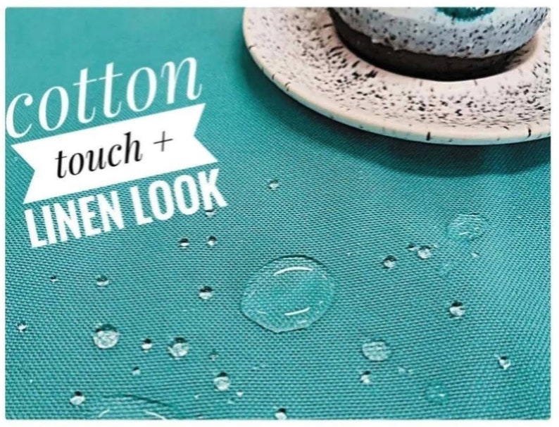 Op de afbeelding: Een close-up van een turquoise tafelkleed met waterdruppels. De tekst "cotton touch + LINEN LOOK" staat in het wit. Een witte schotel met een zwart gespikkelde rand en een kopje zijn zichtbaar.