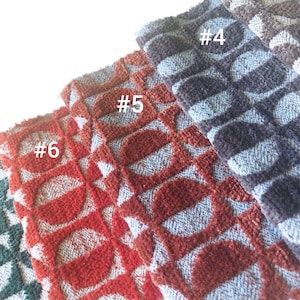 May include: Close-up of several fabric swatches with a repeating geometric pattern. The swatches are in shades of red, blue, and gray. The pattern consists of circles within a diamond grid. The fabric has a textured, plush appearance.