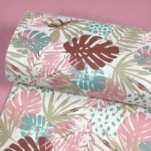 Pode incluir: Um rolo de tecido com um padrão de folhas tropicais. O design apresenta folhas grandes e estilizadas em tons de rosa, azul-petróleo, castanho e bege sobre um fundo branco. O tecido está enrolado, mostrando o padrão repetido.