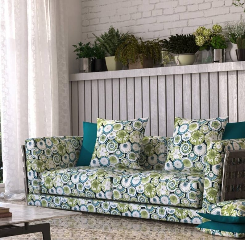 May include: A green and white patterned sofa with two green and white patterned throw pillows and a teal throw pillow. The sofa is in front of a white brick wall with a wooden shelf above it.