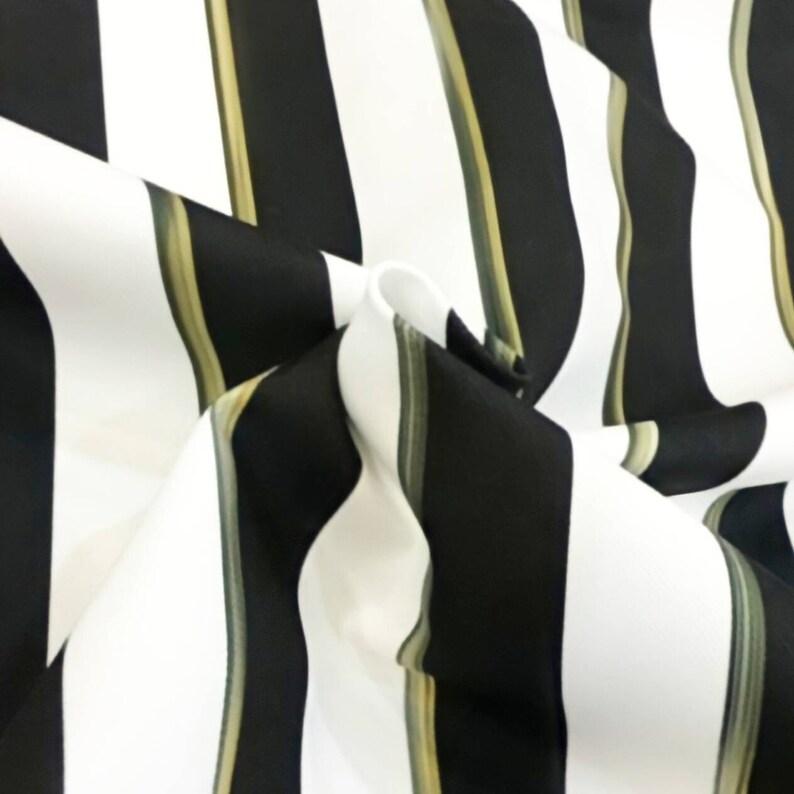 May include: Close-up of a fabric with a bold striped pattern. The design features alternating vertical stripes of black and white, with thin olive green stripes. The fabric is folded, creating depth and texture.