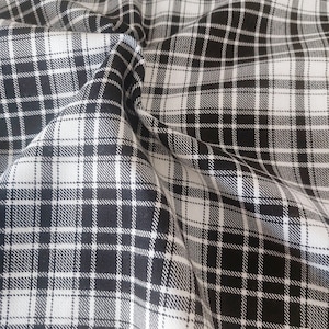 Pode incluir: Tecido xadrez preto e branco com textura tecida. O tecido está dobrado e enrugado, mostrando o padrão e a textura.