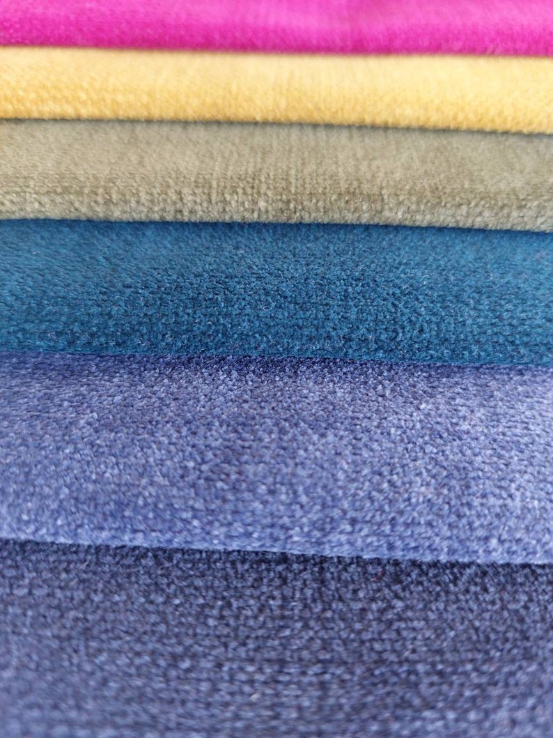 May include: A stack of six fabric swatches in various shades of blue, gray, yellow, and pink. The fabric has a soft, fuzzy texture.