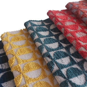 May include: Close-up of several folded fabric pieces in various colors. The fabrics feature a repeating geometric pattern of half-circles in shades of navy blue, yellow, teal, red, and rust. The texture appears to be a woven or looped design.