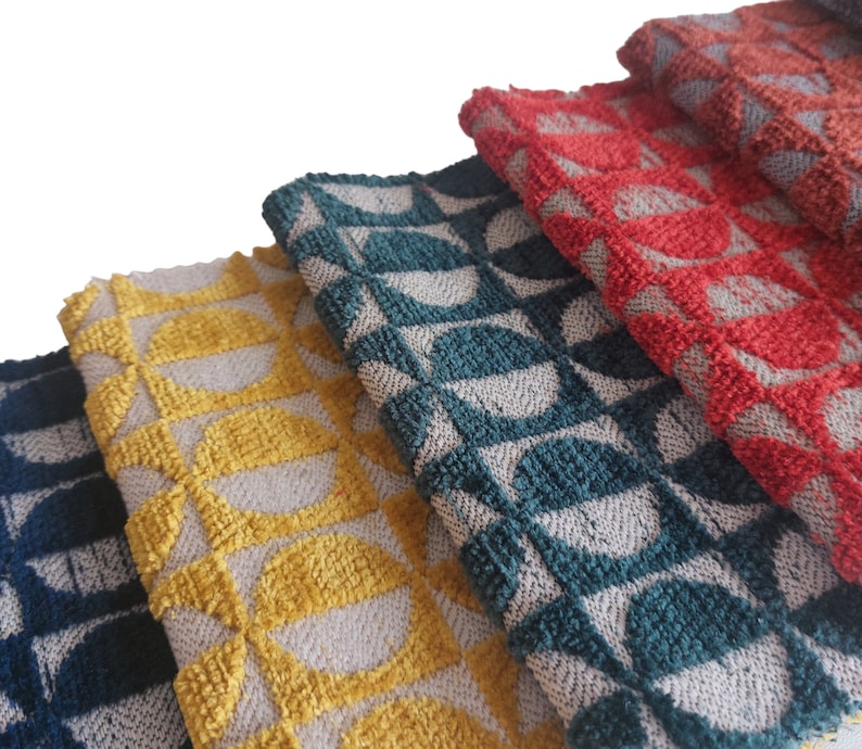 May include: Close-up of several folded fabric pieces in various colors. The fabrics feature a repeating geometric pattern of half-circles in shades of navy blue, yellow, teal, red, and rust. The texture appears to be a woven or looped design.