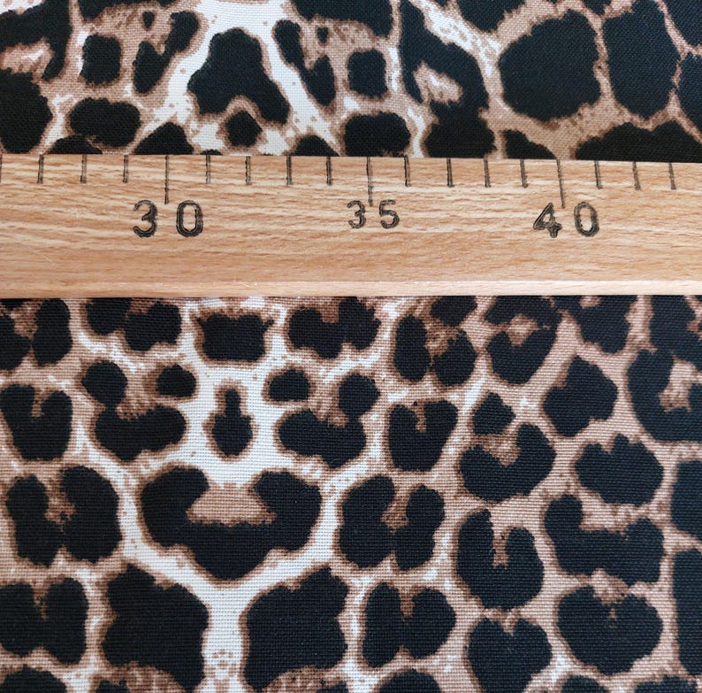 May include: A fabric featuring a repeating leopard print pattern in shades of black, brown, and tan. A wooden ruler is placed horizontally across the fabric, showing markings from 30 to 40 centimeters to indicate the scale of the print design.