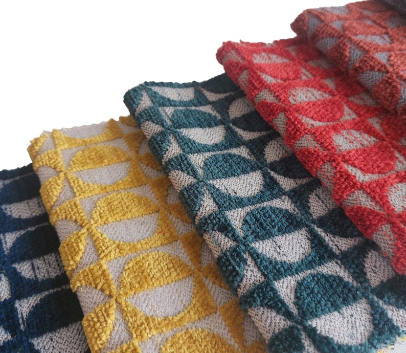 May include: Close-up of several folded towels in various colors, including yellow, teal, red, and navy. Each towel features a repeating geometric pattern of half-circles in a contrasting color, creating a textured appearance. The towels are made of a soft, woven material.