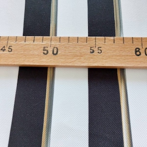 May include: Close-up of a fabric with vertical stripes in black and white. A wooden ruler is placed across the fabric, with measurements in inches. The fabric has a textured appearance.