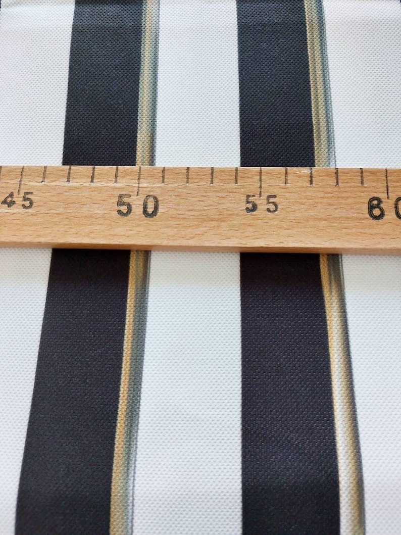 May include: Close-up of a fabric with vertical stripes in black and white. A wooden ruler is placed across the fabric, with measurements in inches. The fabric has a textured appearance.