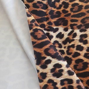 May include: Close-up of a brown and black leopard print fabric with a white fabric underneath.