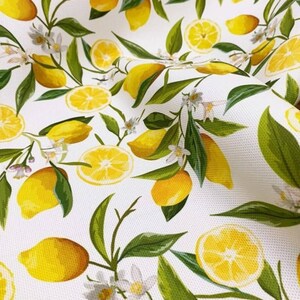 K&ouml;nnte beinhalten: Wei&szlig;er Stoff mit einem sich wiederholenden Muster aus gelben Zitronen, gr&uuml;nen Bl&auml;ttern und wei&szlig;en Bl&uuml;ten. Einige Zitronen sind ganz, andere sind halbiert. Das Design erinnert an einen Sommergarten.