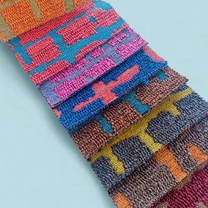 Könnte beinhalten: Eine Sammlung farbenfroher, strukturierter Stoffmuster. Die Muster weisen ein sich wiederholendes geometrisches Muster in Orange-, Rot-, Blau-, Rosa-, Braun- und Gelbtönen auf. Die Stoffe sind diagonal angeordnet und zeigen die Farb- und Texturvielfalt.