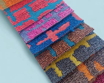 May include: A collection of colorful, textured fabric samples. The samples feature a repeating geometric pattern in shades of orange, red, blue, pink, brown, and yellow. The fabrics are arranged in a diagonal row, showcasing the variety of colors and textures.
