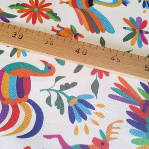 May include: White fabric with a colorful repeating pattern of stylized birds, flowers, and geometric shapes. A wooden ruler is placed on top of the fabric, with the numbers 25, 30, 35, 40, 45, 50, and 55 visible.