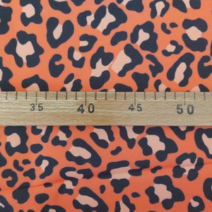 May include: Orange fabric with a black leopard print pattern. A wooden ruler with markings in inches is placed on top of the fabric. The ruler shows measurements from 35 to 50 inches.