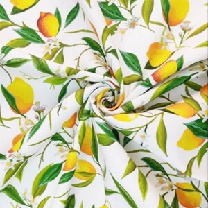 K&ouml;nnte beinhalten: Wei&szlig;er Stoff mit einem sich wiederholenden Muster aus Zitronen, gr&uuml;nen Bl&auml;ttern und wei&szlig;en Bl&uuml;ten. Die Zitronen sind gelb und orange, und die Bl&auml;tter sind gr&uuml;n. Der Stoff ist gewirbelt und zeigt das sich wiederholende Muster.