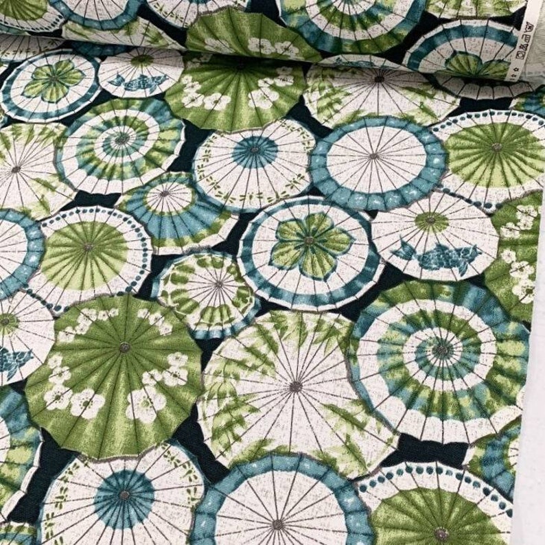 May include: A fabric with a repeating pattern of green and white umbrellas on a dark blue background.