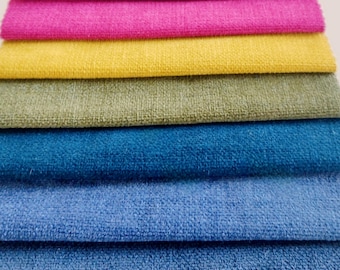 Pode incluir: Uma pilha de amostras de tecido em várias cores, incluindo roxo, rosa, amarelo, verde, azul e azul claro. O tecido tem uma superfície texturizada.