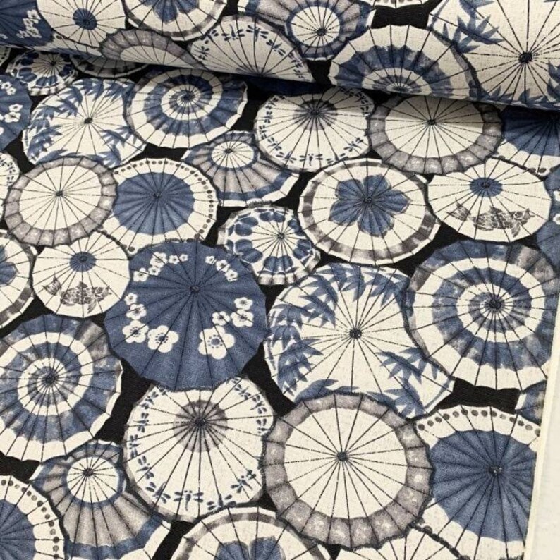 May include: A black fabric with a repeating pattern of blue and white umbrellas. The umbrellas are various sizes and have different designs, including floral and geometric patterns.