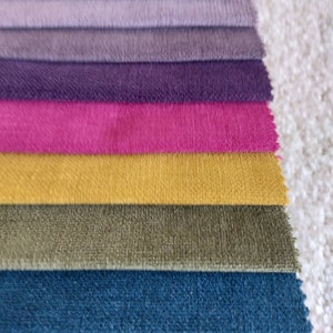 May include: A stack of fabric swatches in various shades of purple, pink, yellow, green, and blue. The swatches are arranged in a gradient from dark to light.